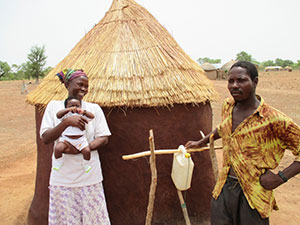 Women, man and baby standing outside a hut
