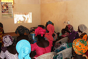 Community members gather at their local health facility to watch a video on best practices for complementary feeding.