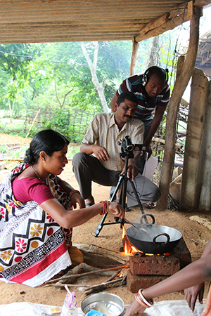 Photo of two men filming a woman cooking in a pot