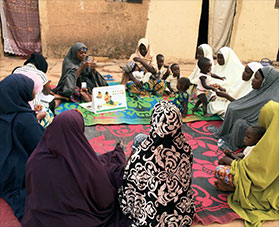 Women sit on rugs and discuss behavior change.