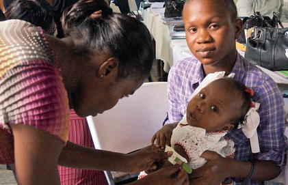 A health workers bends down to touch a baby in her mother's arms.