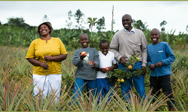A family standing in a field holding fruit