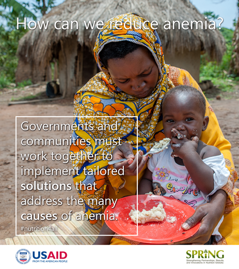 A woman sits on the ground with a hut in the background. She leans over and focuses intently on her baby whom she is attempting to feed. The baby is more interested in the camera than in the food. The overlay text says: How can we reduce anemia? Governments and communities must work together to implement tailored solutions that address the many causes of anemia.