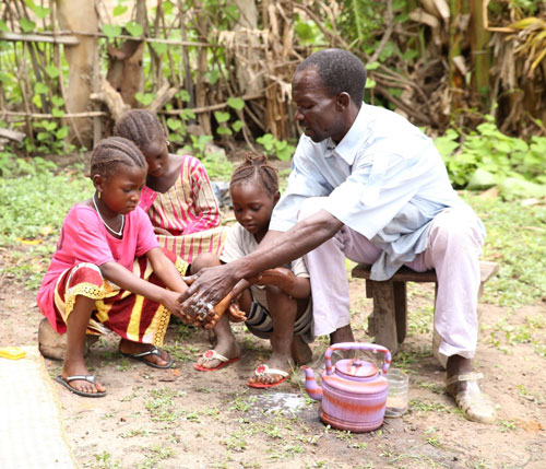A father helps his children learn to wash their hands.