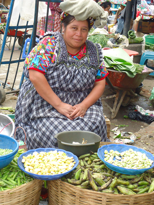 Photo of a woman sitting at her produce stall in an outdoor market.