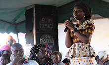 Mariam Sy, SPRING/Senegal Nutrition Advisor, holds a microphone on stage in both hands and addresses the crowd gathered.