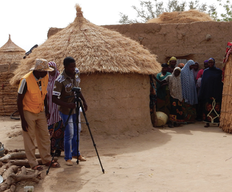 Photo of video crew and villagers outside a hut.