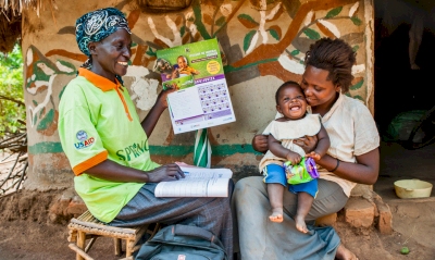 Photo of community health worker showing a mother (holding her young child) the MNP calendar