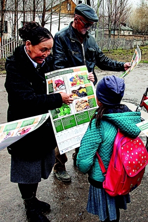 Photo of a woman showing a poster on nutrition to a young girl and her grandparent