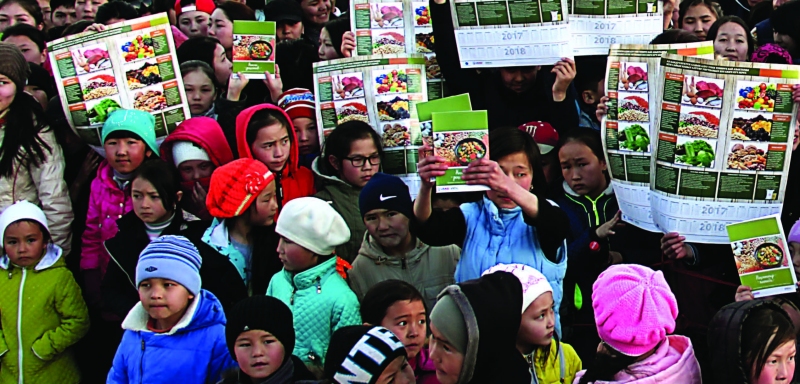 Photo of about thirty or so women and girls, some of whom are holding up posters on nutrition
