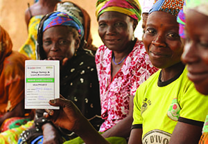 Photo of a group of women sitting, one of whom is holding up a form with USAID|Ghana and SPRING logos titled 