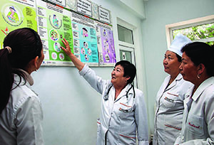 Photo of a health care supervisor instructing three health care workers and pointing to a poster on breastfeeding. 