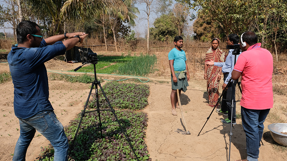 A couple talks to a visitor about growing Indian spinach. The couple explains that their Indian spinach sells quickly in the market. Consumers know how the spinach is grown and that the plant is nutritious. Photo credit: Sarah Hogan, 2017