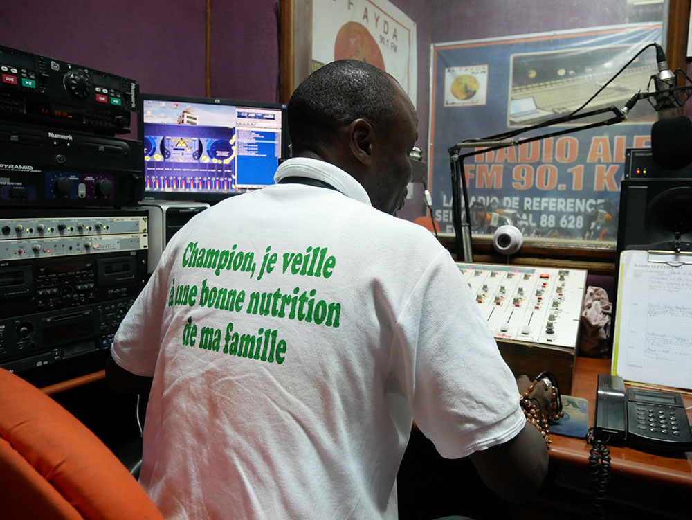 A radio DJ wearing a shirt with SPRING’s messaging produces a radio program on water, sanitation, and hygiene at Al Fayda FM in Kaolack.