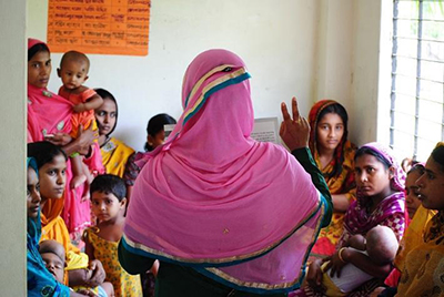 Photo of a woman speaking to a group of women and children. 