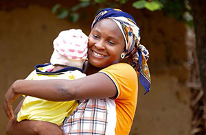 A woman smiles at the camera while holding her baby.