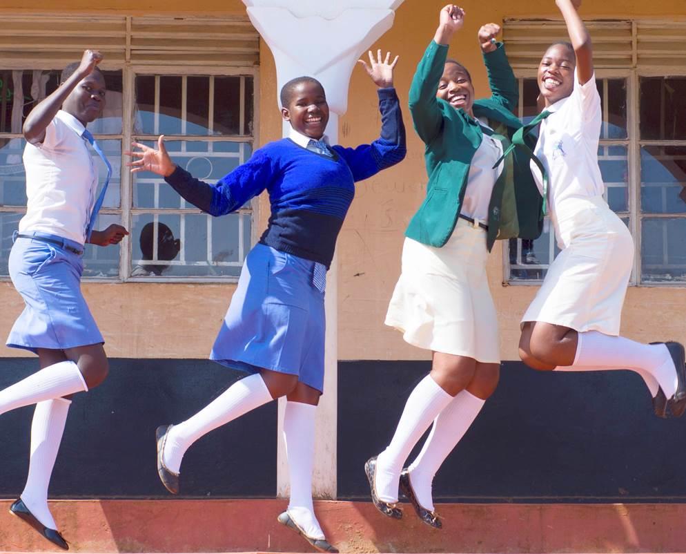  four teenage girls in their school uniforms, dancing and jumping as they pose for the camera. 