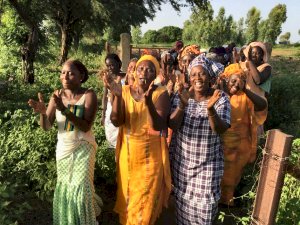 Photo of a group of women walking through a garden singing and clappingn hands.