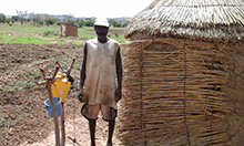 Photo of a man, Tengdo Kuzoba, standing by his latrine and tippy tap.