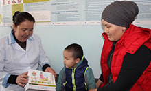 Photo of a mother, her child, and a nurse at a health facility looking at information on nutrition. Caption: "Mairam Usupova, Head Nurse at the Family Group Practice in Naryn, counsels a mother on maternal nutrition and dietary diversity.