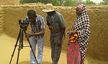 One man looking into a camera on a tripod while a man and woman watch