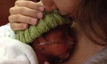 Kristina holds and kisses the head of her premature infant, who has an oxygen tube in his nose.