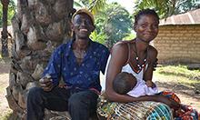 Photo of a man and woman posing outside with their infant child