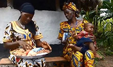A mother prepares healthy food for her baby. The grandmother, holding the fussy baby, looks on.