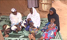 Health worker and two new mothers sitting on a rug and talking