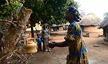 A woman washes her hands at a tippy tap hung from a tree branch