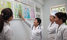 Photo of a group of women in medical coats pointing to charts on a wall.
