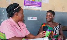 Two women sit and talk. One woman holds a packet of micronutrient powder and explains its benefits to the other woman.