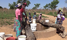 Photo of a group of women and children at a water well, collecting water in buckets. 
