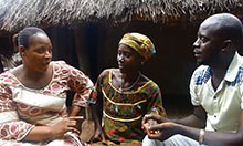 A health worker, pregnant woman, and the pregnant woman's husband sit together on a bench and talk.