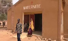A husband walks several steps ahead of his wife as they exit a maternity health clinic.