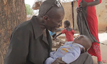 A father grins at his infant. He holds the baby in his lap and supports its neck.
