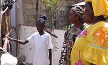 Three older women watch as a school-aged girl shows them how to use a tippy tap.