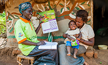 Photo of community health worker showing a mother (holding her young child) the MNP calendar