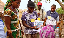 Photo of a group of women and men gathering to look at a flyer on handwashing. 
